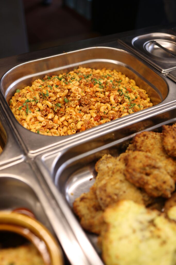 Mouth-watering macaroni pasta and fried food in warm buffet trays.