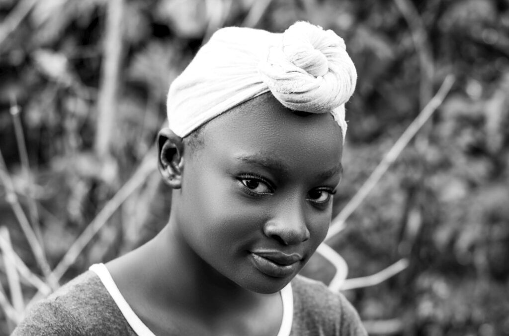 A grayscale close-up of a smiling girl with a headwrap, capturing innocence and beauty.